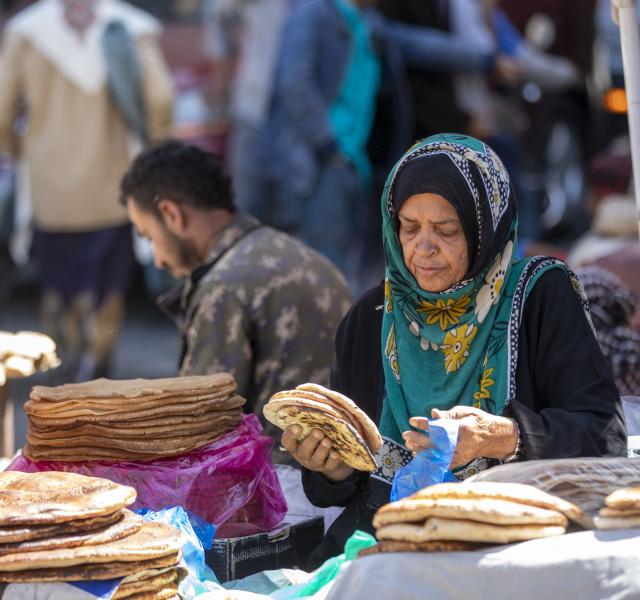 Misk Mohammed, 70, sells bread to a customer at a market in the Taiz Governorate.