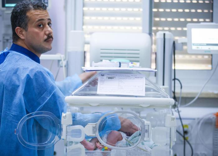 A man standing next to an incubator with his hand on the baby inside