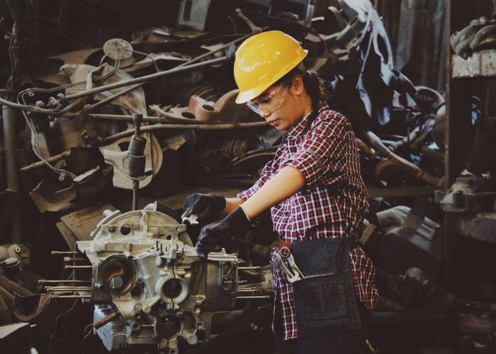Woman with protective gear working on a piece of machinery